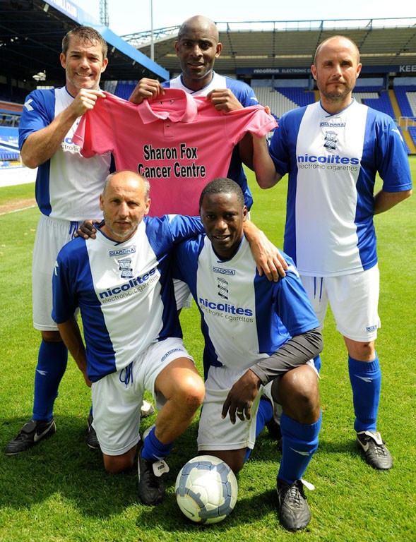 Football team standing on the pitch holding a jersey for the Sharon Fox Cancer Centre.